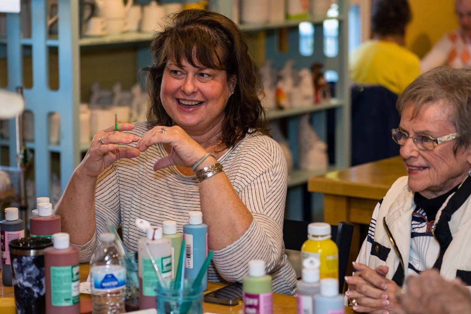 Two women smiling and talking while painting pottery at Pottery Bayou in Winona Lake, IN