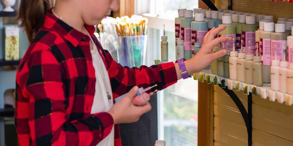 Girl with brown hair choosing paint colors to paint her own pottery at Pottery Bayou in Winona Lake, IN