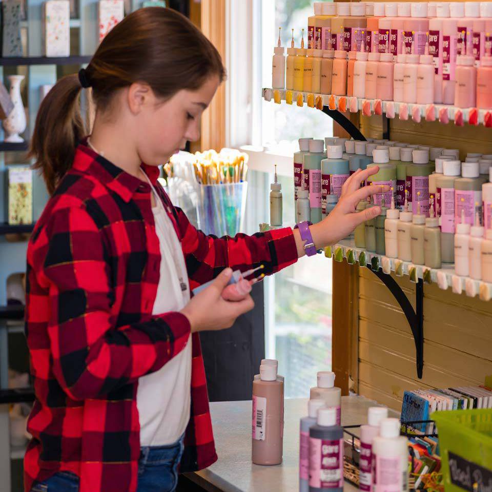 Girl with brown hair choosing paint colors to paint her own pottery at Pottery Bayou in Winona Lake, IN