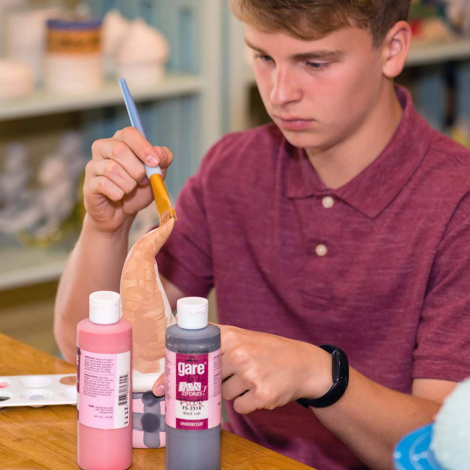young adult using a large paintbrush to customize his make-your-own pottery gnome at Pottery Bayou in Winona Lake, IN