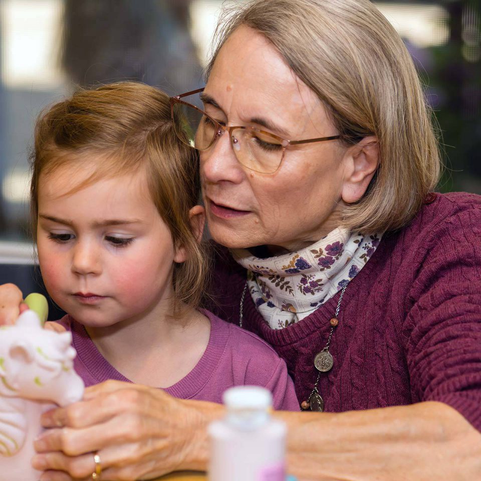 older woman with glasses helping a young child paint a clay unicorn at Pottery Bayou