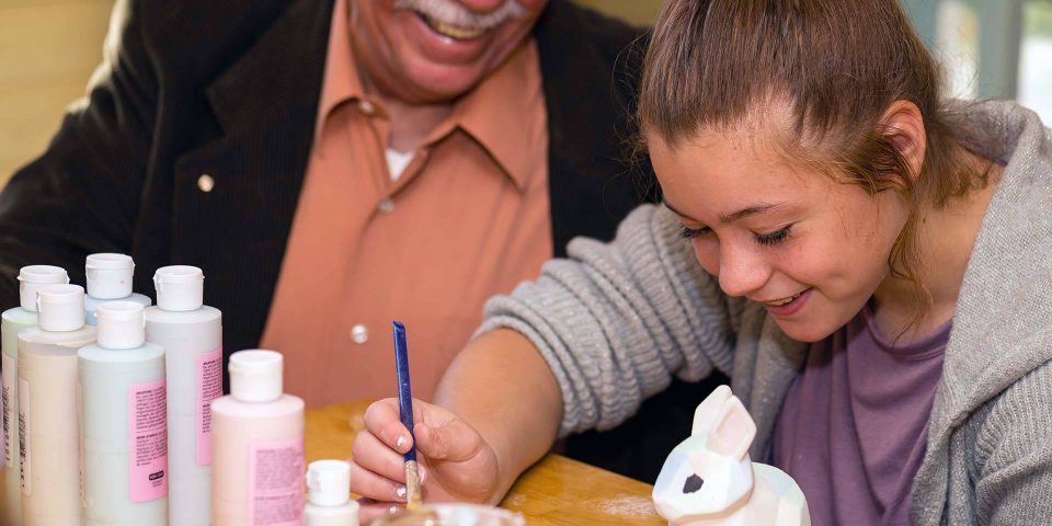 Older man smiling at younger woman painting her own pottery rabbit using a palette and paint brush
